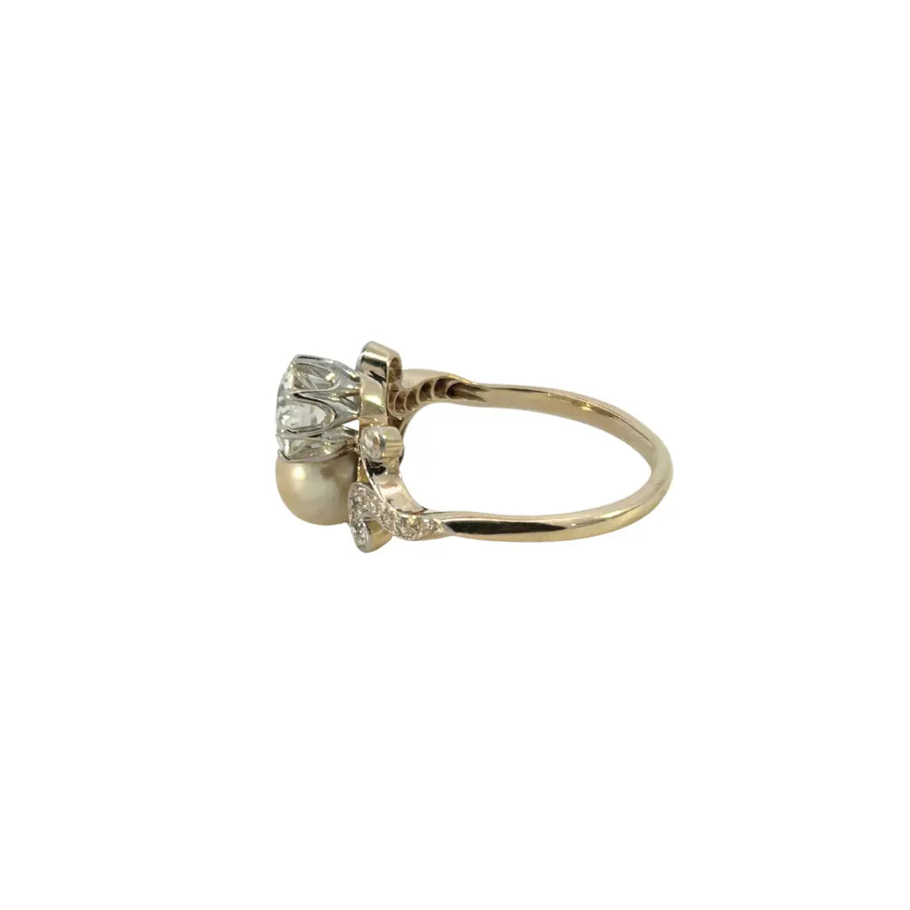 Angled view of Edwardian two-stone diamond and pearl ring with bead-set swirl accents.