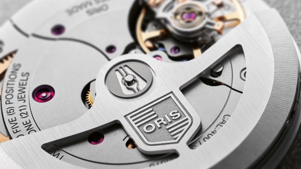 Oris Aquis watch with a striking blue dial, stainless steel case, and a unidirectional rotating bezel, showcasing its sleek design and robust functionality. Close up view of mechanism on back.