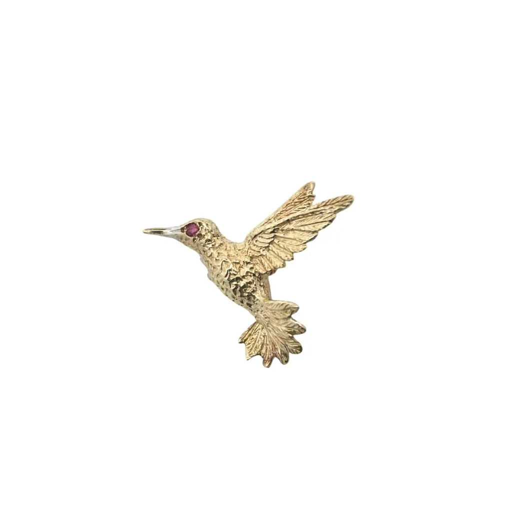 Front view of a yellow gold hummingbird pin featuring sculpted wings and a ruby gemstone eye.