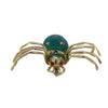 Front-facing view of a gold spider brooch with green guilloché enamel and red eyes.