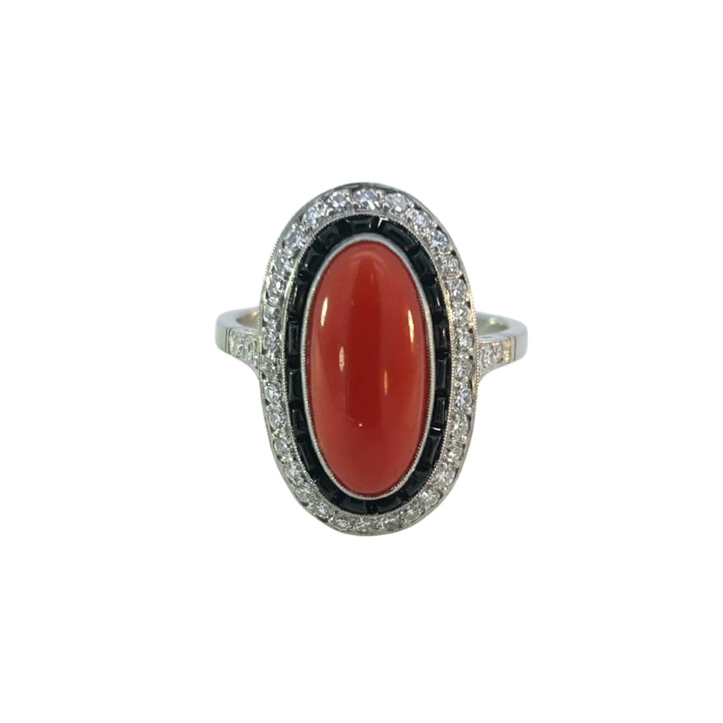 Front view of a platinum Art Deco ring with an elongated red coral center, surrounded by calibré-cut onyx and diamond halo.