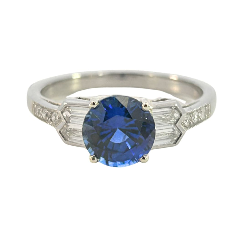 Front view of a platinum ring with round blue sapphire and tapered baguette diamond shoulders.