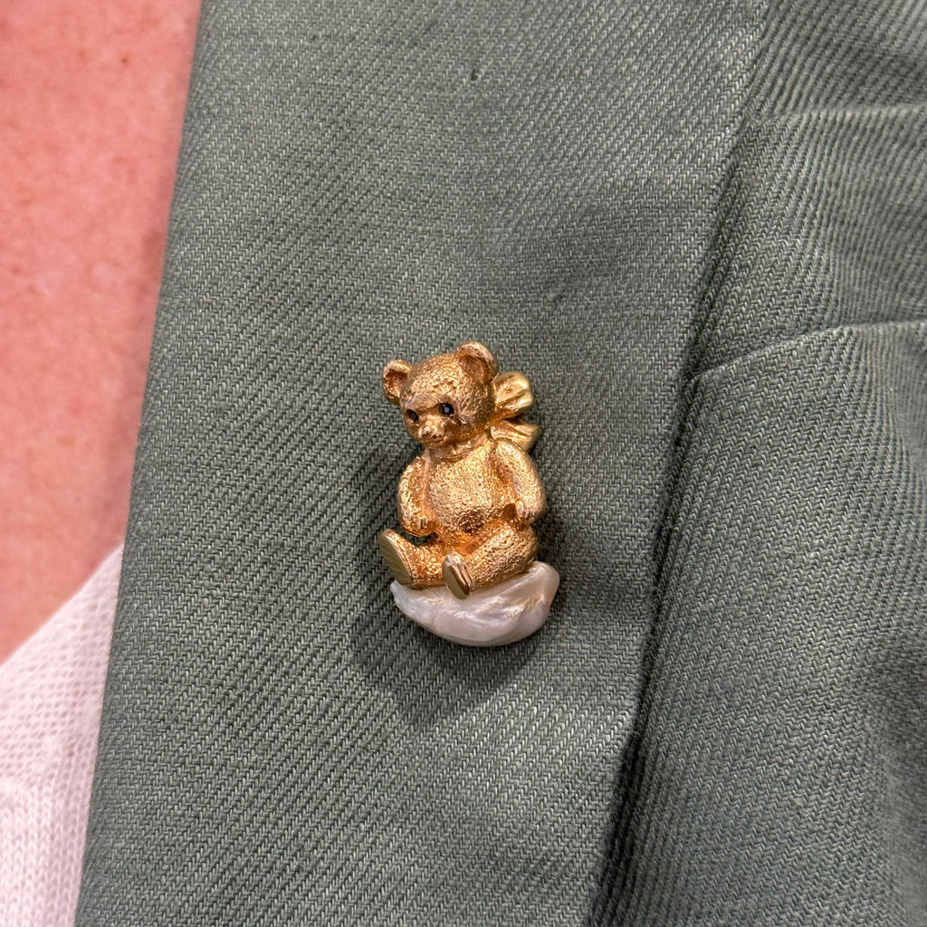 On mod view of William Ruser teddy bear brooch in 14k yellow gold with sapphire eyes seated on an American freshwater pearl.l
