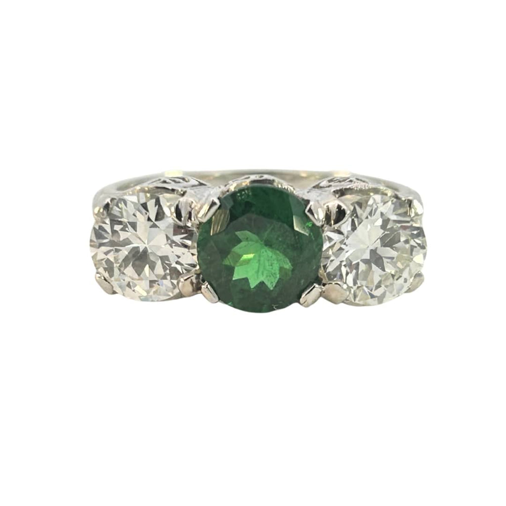 Three-stone ring with 1.63ct green tsavorite flanked by two round diamonds in an engraved white-metal mount.