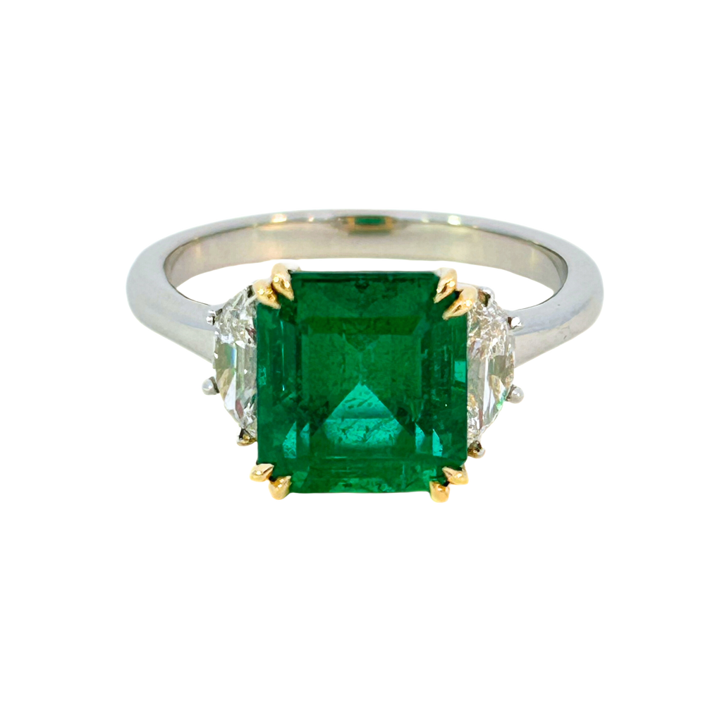 Front view of a three-stone ring featuring a 3.03 ct Zambian emerald flanked by half-moon diamonds in an 18k yellow gold and platinum setting.